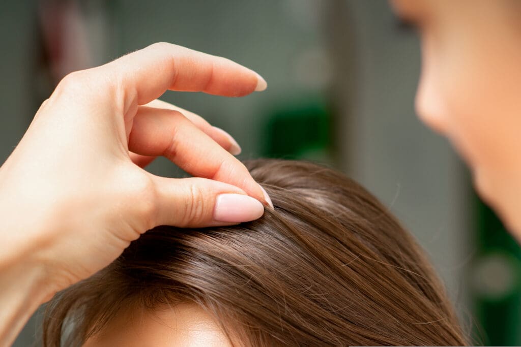 A hairdresser is making the hairstyle of a young brunette woman in a hair salon, close up.